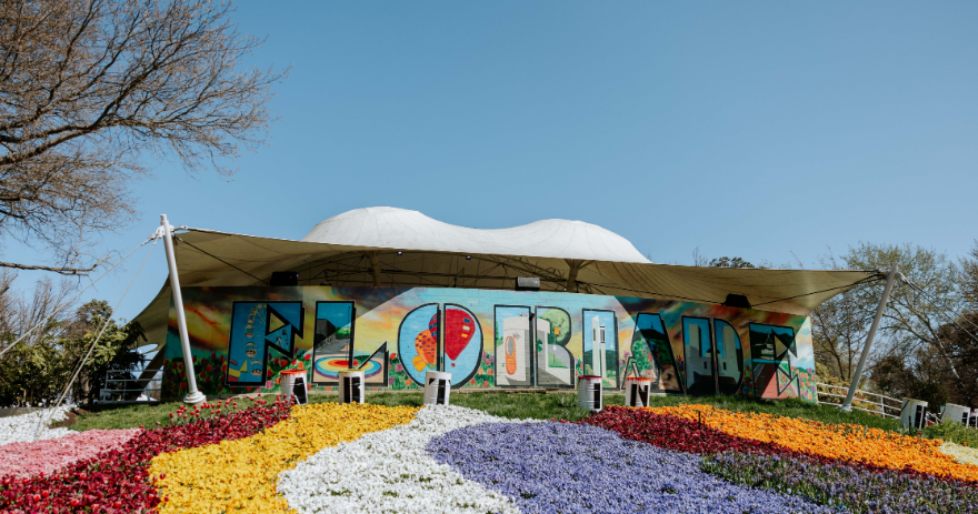 “Floriade” sign displayed across a building façade, with patterned flower beds in yellow, white and purple in the foreground.