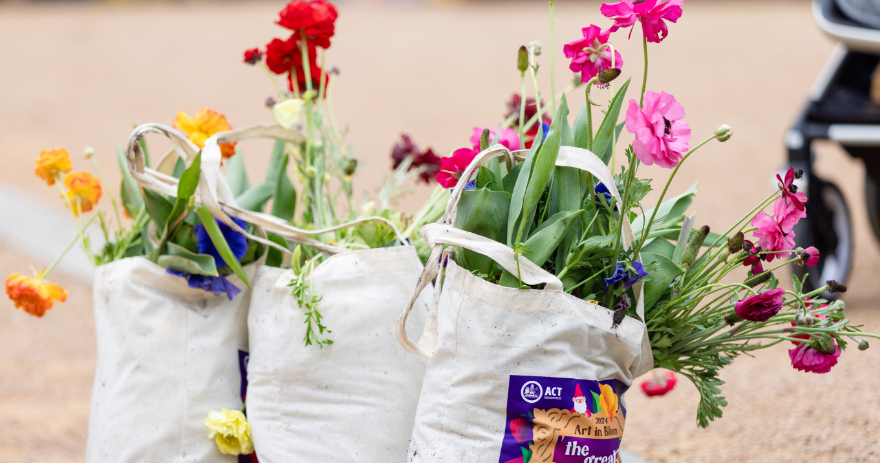 Three canvas bags filled with mixed flowers and greenery placed on the ground.