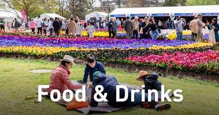 Food and Drinks, people on a picnic rug near colourful flower beds and food stalls at Floriade.