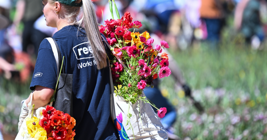 A woman carrying two bags over their shoulder full of flowers through a garden