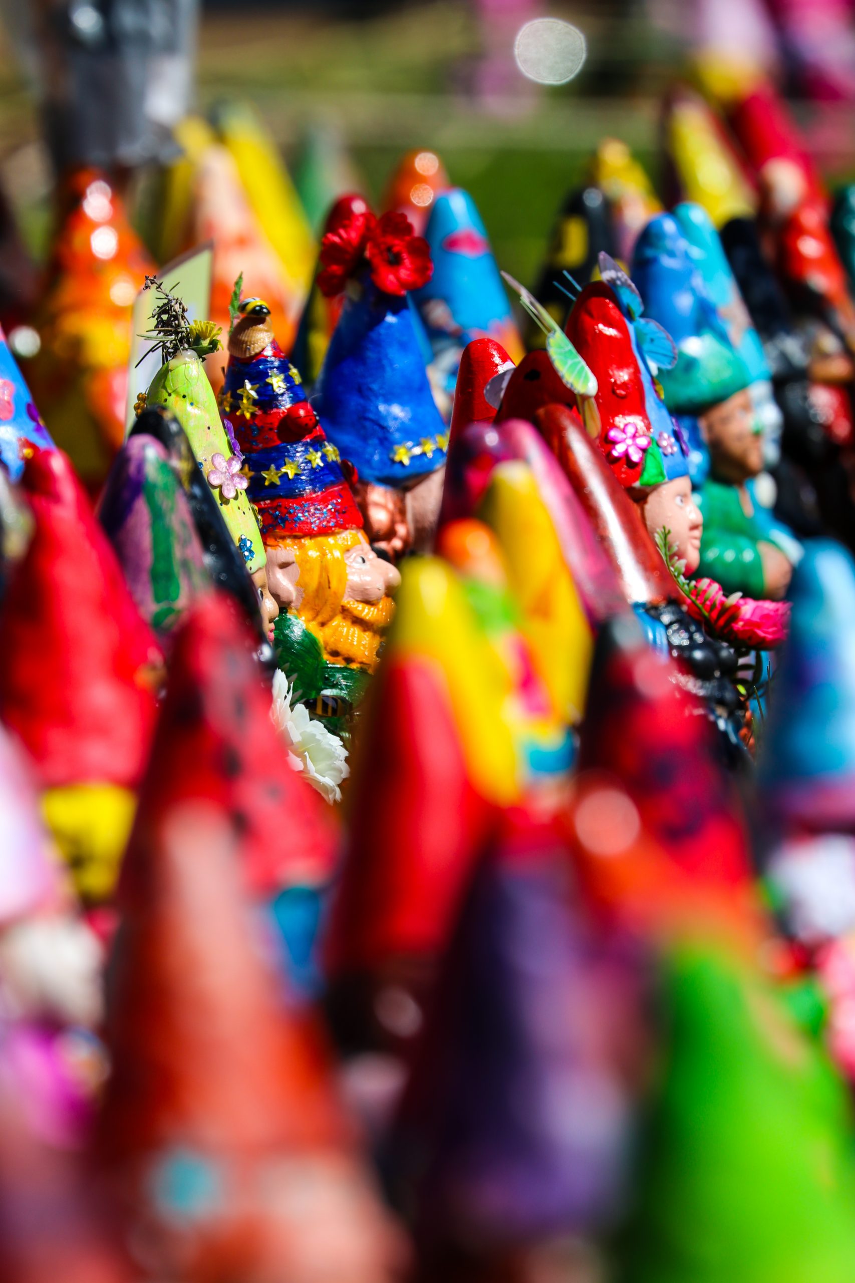 Close-up of colourful painted gnomes in bright rainbow colours, with rows of gnomes blurred in the background.