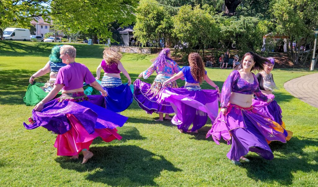 Bellydance group dancing in bright purple costumes on grass