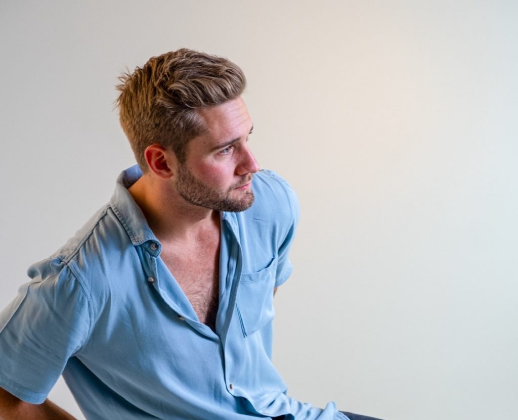 Studio-style portrait of a person wearing a light blue button-up shirt and looking to the side against a clean white background.