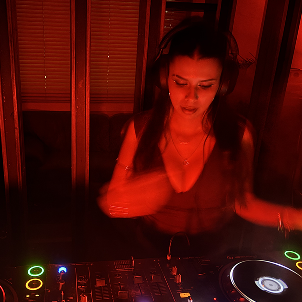 DJ performing on stage with red lighting and a DJ deck in front