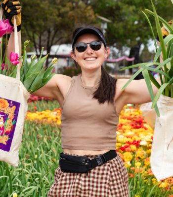 Person wearing gloves holds two large bags filled with flowering plants while standing in a vibrant tulip garden.