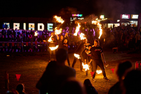 Fire performers spin flaming batons in front of a large crowd, with the illuminated “FLOREADE” sign visible in the background at night.