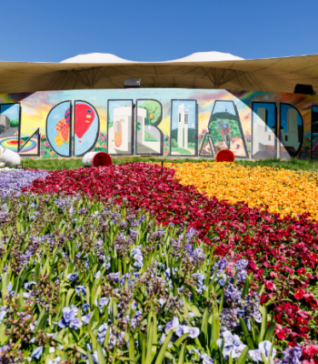 “Floriade” sign displayed across a building with large, patterned flower beds in purple, red, orange and yellow in the foreground.