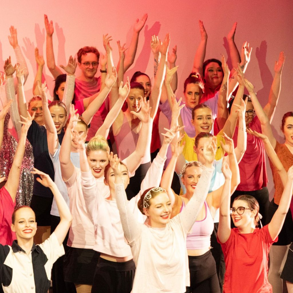 This photo is of a group of young adults with their hands in the air during a dance routine.
