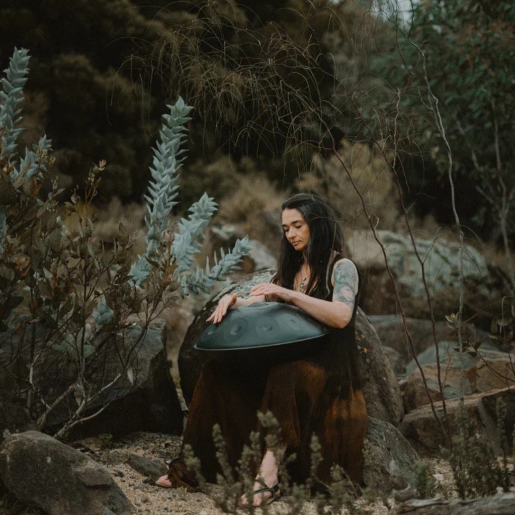 woman with brown hair in Australian bush holding a sound bath instrument