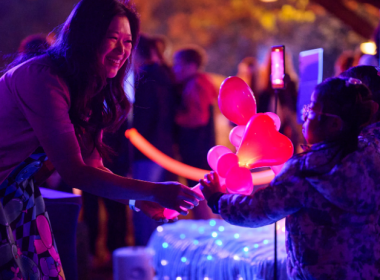 Visitors interact with a colourful illuminated installation during a night-time festival experience.