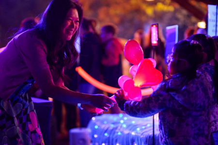 Visitors interact with a colourful illuminated installation during a night-time festival experience.