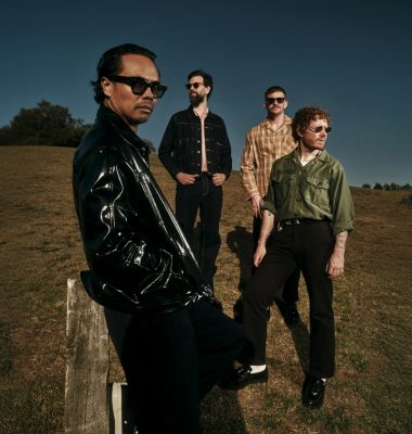 A four-piece band poses outside in a paddock