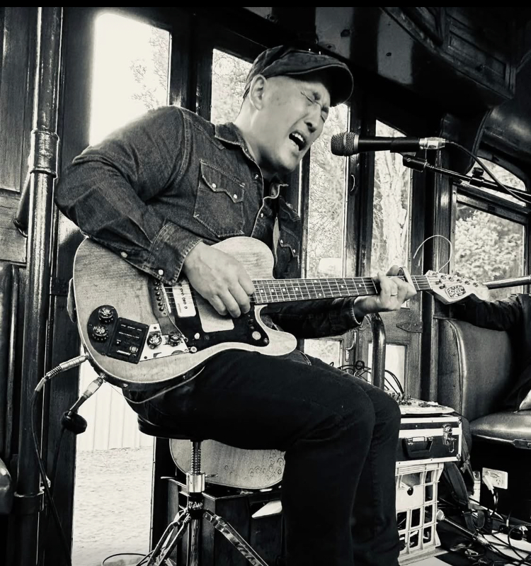 Musician playing an electric guitar and singing into a microphone in a vintage rail carriage.