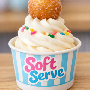 Donnut puff Balls cup of vanilla soft serve ice cream topped with rainbow sprinkles and a sugar-coated doughnut ball, served in a blue-and-white striped branded cup.