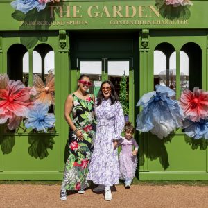 Visitors pose in front of The Garden, a bright green festival installation decorated with oversized floral decorations and garden-inspired styling.