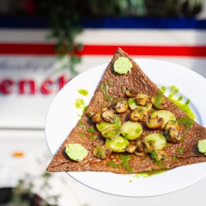 Savory French crepe topped with sliced zucchini and mushrooms, served on a white plate in front of Le Petit Brenton food truck.