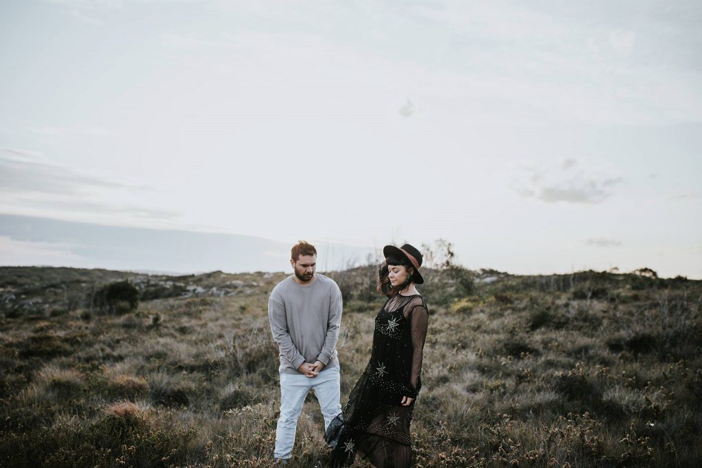Two performers standing in an open grassland landscape beneath a cloudy sky.