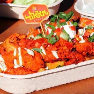 Loaded fries topped with tandoori-style chicken, sauces, sour cream, and spring onions, served in a takeaway tray from Tikka Stand.