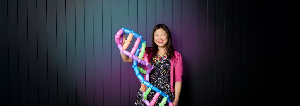 Performer holding a colourful balloon sculpture against a dark panelled backdrop.