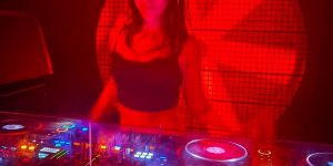 DJ performing on stage with red lighting and a DJ deck in front